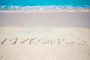 parola mykonos manoscritto su sabbioso spiaggia con morbido oceano onda su sfondo foto