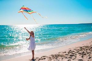 bambina che pilota un aquilone sulla spiaggia al tramonto foto