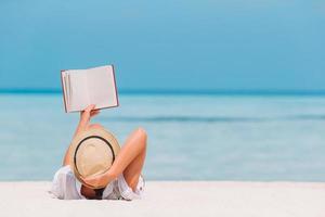 ritratto di un' giovane donna rilassante su il spiaggia, lettura un' libro foto