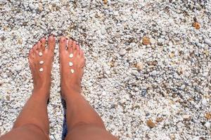 gambe femminili con ciottoli sulla spiaggia di sabbia bianca foto