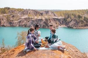 giovane genitori e bambini su picnic dopo escursioni a piedi nel montagne. bellissimo Visualizza di blu lago foto