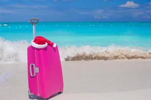 avvicinamento di rosa bagaglio e Santa Claus cappello su tropicale spiaggia foto