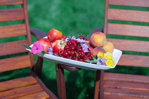 piatto con fresco frutta e fiori su di legno sedie nel il giardino foto
