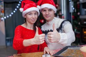 giovane contento coppia nel Natale cappello sollevato pollici su a casa foto