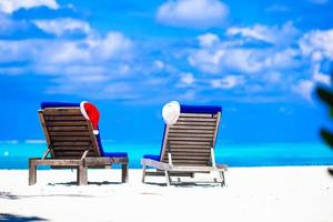 Natale concetto, spiaggia lettini con rosso Santa e cannuccia cappelli sfondo bellissimo turchese mare foto