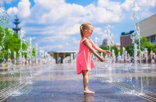 poco ragazza giocando nel Aperto strada Fontana a caldo soleggiato giorno foto