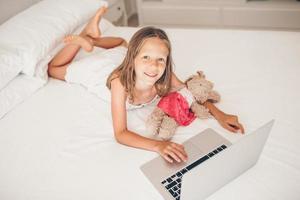 carino poco ragazza fare compiti a casa su il computer portatile foto