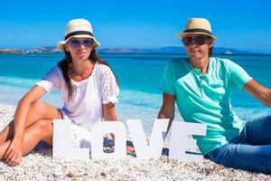 giovane famiglia seduta su il spiaggia con parola amore foto