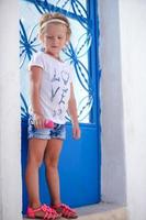 adorabile poco ragazza in piedi vicino blu porta di vecchio Casa nel emporio villaggio, santorini, Grecia foto