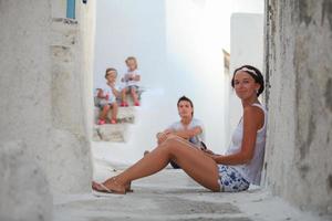 giovane madre sfondo sua carino figlie e marito nel un' greco villaggio su il Cicladi isole foto