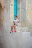adorabile poco ragazza seduta su il passaggi di vecchio Casa nel emporio villaggio, santorini, Grecia foto
