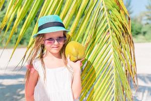 poco adorabile ragazza con grande Noce di cocco su bianca sabbioso spiaggia foto