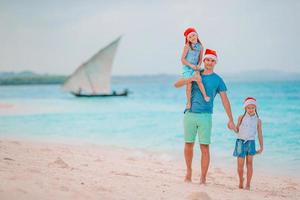 contento famiglia nel rosso Santa cappelli su un' tropicale spiaggia festeggiare Natale vacanza foto