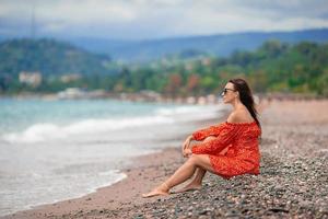 giovane contento donna su il spiaggia con montagna Visualizza foto