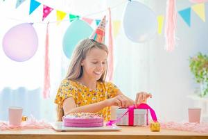 caucasico ragazza è sognante sorridente e guardare a compleanno arcobaleno torta. festivo colorato sfondo con palloncini. compleanno festa e auguri concetto. foto