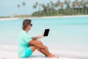 giovane uomo con il computer portatile a tropicale spiaggia vicino acqua villa foto