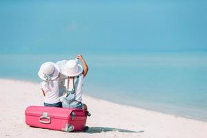 poco ragazze con grande valigia e carta geografica a tropicale spiaggia foto