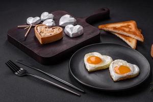 Due a forma di cuore fritte uova su un' nero ceramica piatto su un' buio calcestruzzo sfondo foto