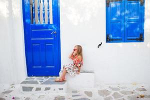 poco ragazza all'aperto nel vecchio strade un mykonos. ragazzo a strada di tipico greco tradizionale villaggio con bianca muri e colorato porte su mykonos isola, nel Grecia foto