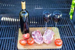 Due bicchiere di rosso vino, bistecca e pomodori su barbecue all'aperto foto