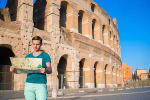 contento tipo con carta geografica nel davanti di colosseo. giovane uomo ricerca il attrazione sfondo il famoso la zona nel Roma, Italia foto