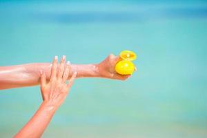 mani femminili con la bottiglia di crema solare sfondo blu mare foto