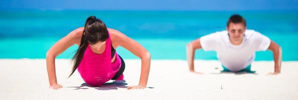 giovane fitness coppia fare sollevamento durante all'aperto attraversare formazione allenarsi su tropicale spiaggia foto