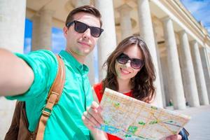 giovane turista amici in viaggio su vacanze nel Europa sorridente contento. caucasico famiglia con città carta geografica fabbricazione autoscatto sfondo di attrazioni foto