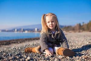 adorabile poco ragazza su il spiaggia nel un' accogliente maglione e vestito a caldo inverno giorno foto