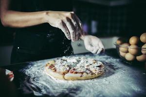 mani dello chef che versano farina sulla pasta cruda foto