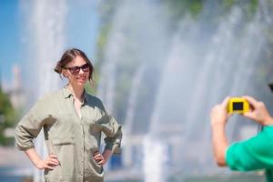 giovane uomo assunzione un' immagine di il suo fidanzata mentre seduta sfondo il Fontana. giovane uomo fabbricazione foto di donna su il strada ridendo e avendo divertimento nel estate.