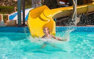 poco ragazza su acqua diapositiva a Parco acquatico durante estate vacanza foto