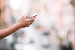 avvicinamento di femmina mani Tenere cellulare all'aperto su il strada. donna utilizzando mobile smartphone. foto