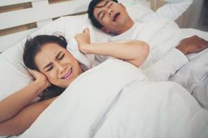 donna che dorme bloccando le orecchie con l'uomo che russa a letto foto