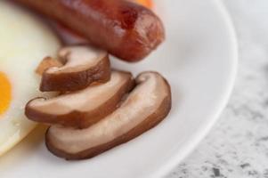 colazione composta da pane, uova fritte, pomodori, salsiccia cinese e funghi. foto