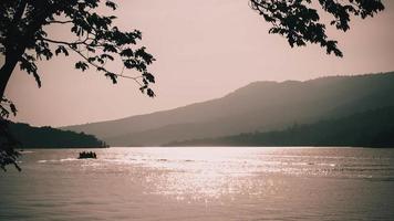 riflessione della luce dalle onde superficiali di un lago al tramonto con sfondo di montagna.