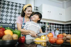 mamma felice e figlia che preparano e tagliano le verdure in cucina foto