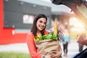 donna dopo shopping nel un' centro commerciale o shopping centro e guida casa adesso con sua auto all'aperto. bellissimo giovane donna shopping nel un' drogheria memorizzare supermercato, mettendo il drogheria in sua auto foto