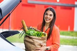 donna dopo shopping nel un' centro commerciale o shopping centro e guida casa adesso con sua auto all'aperto. bellissimo giovane donna shopping nel un' drogheria memorizzare supermercato, mettendo il drogheria in sua auto foto