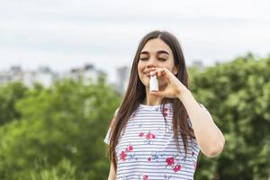 giovane donna utilizzando naso spray per sua polline e erba allergie allergia sollievo fioritura alberi nel sfondo. primavera di stagione allergie e Salute i problemi. foto