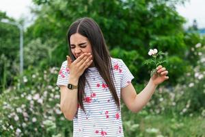 giovane donna con polline allergia Tenere un' fiore e detto NO.. giovane donna con polline e erba allergie. fioritura alberi nel sfondo. primavera di stagione allergie e Salute i problemi. foto