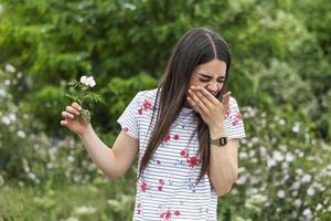 giovane donna con polline allergia Tenere un' fiore e detto NO.. giovane donna con polline e erba allergie. fioritura alberi nel sfondo. primavera di stagione allergie e Salute i problemi. foto