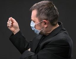 uomo nel medico maschera con un' termometro foto