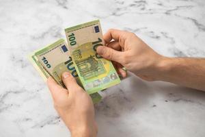 un' uomo conta Euro i soldi con il suo mani su un' leggero sfondo foto