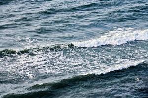 in profondità blu mare acque spruzzi con schiumoso onde, buio blu ondulato oceano acqua superficie, tempestoso mare foto