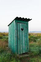 cuore forma su il vecchio di legno gabinetto porta, verde gabinetto nel il campo. all'aperto ricreazione. foto