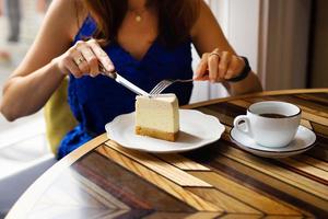 giovane ragazza tagli un' pezzo di crema torta di formaggio, su il sfondo di un' tazza di caffè, avvicinamento. foto