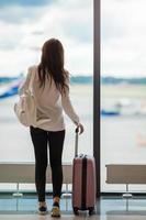 giovane donna vicino grande panoramico finestra nel un aeroporto sala in attesa per arrivo foto