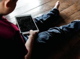 ritratto di un' poco asiatico ragazzo, ragazzo triste viso, infelice bambino seduta Tenere rotto tavoletta computer, emozione triste e triste viso, depresso bambini concetto foto