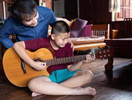 asiatico famiglia bello contento padre e figlio giocando chitarra insieme, padre insegnamento figlio Come per giocare chitarra a casa foto